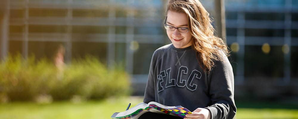 Student reading a textbook near the main building at FLCC's Canandaigua campus