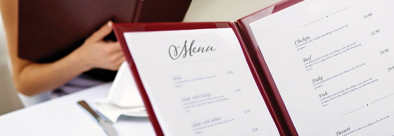 A restaurant menu being handed to a patron sitting at a table