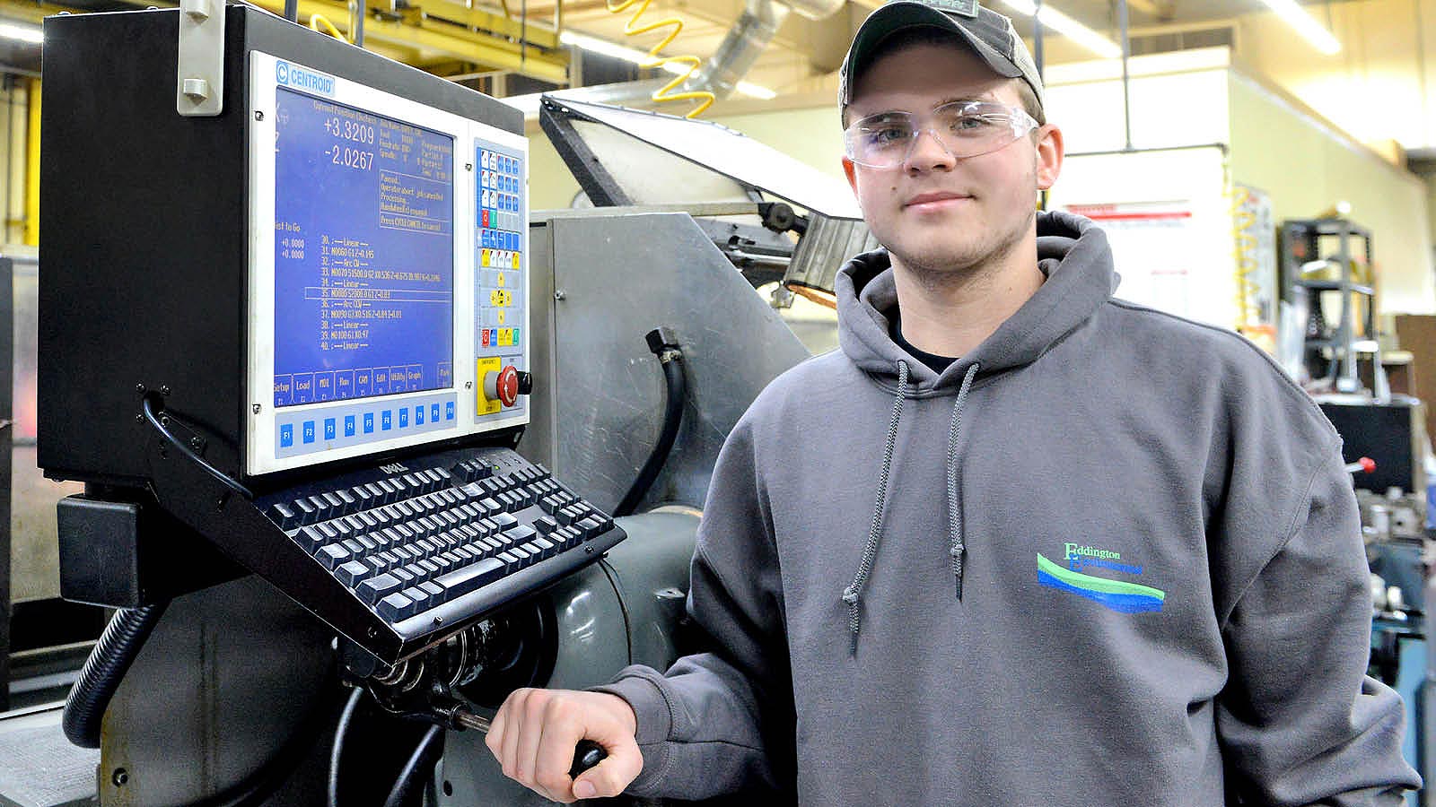 A manufacturing machinist student in front of several pieces of equipment