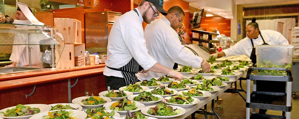 Three culinary students preparing salads to be served during an event.