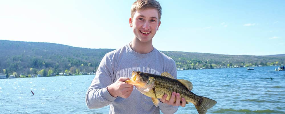 A student holding a fish captured during an FLCC field experience on Canandaigua Lake.