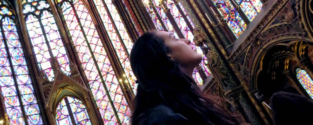 A student standing inside a cathedral admires its stunning architecture during a study abroad trip to France. Light pours through the stained glass windows.
